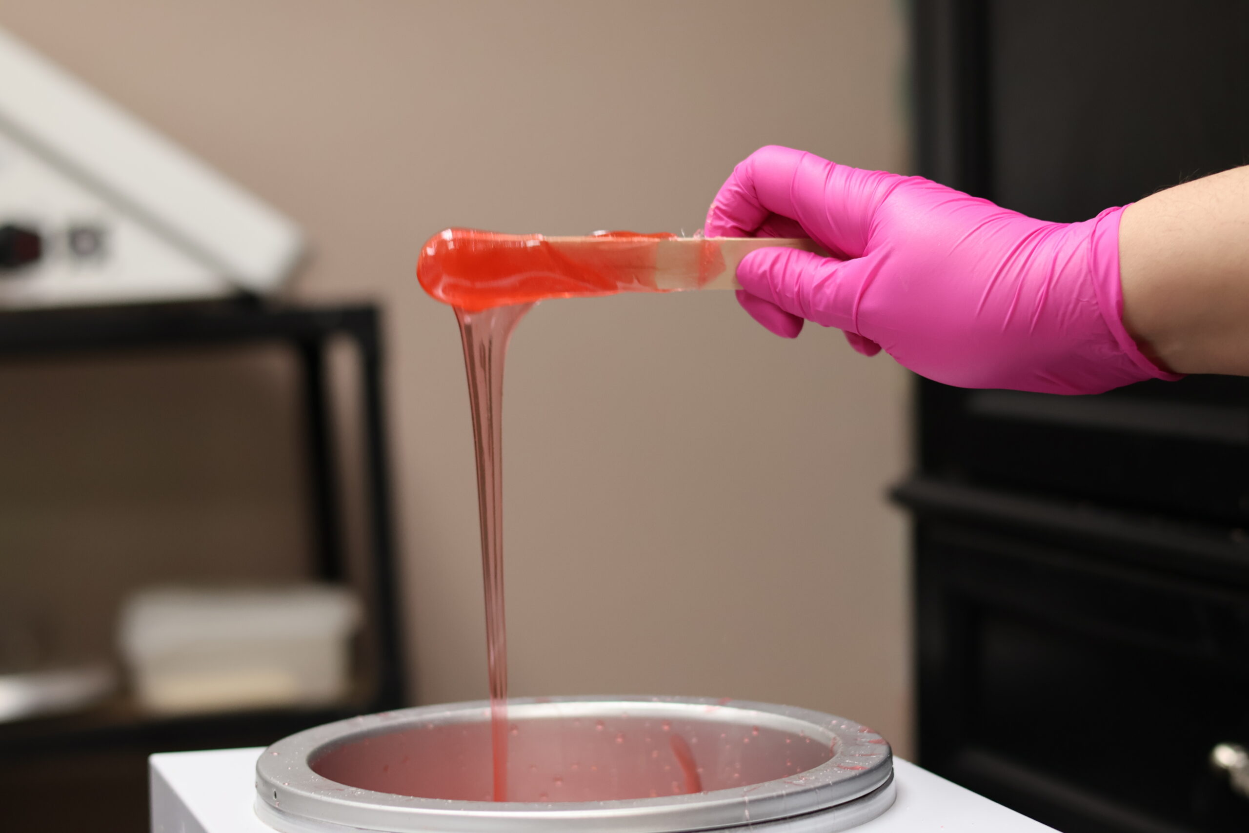 Nikki wearing a pink glove, stretching warm wax from a wax pot.